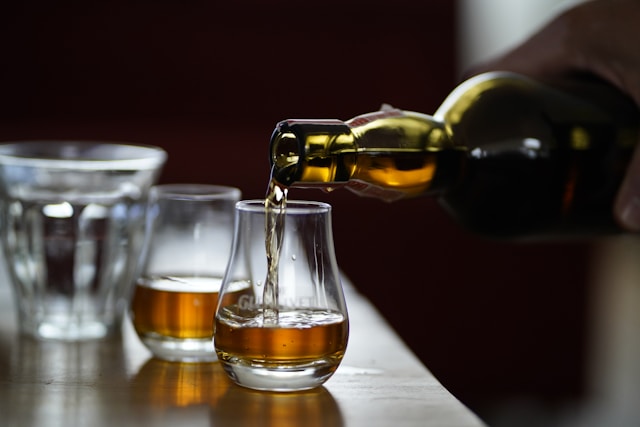 A person pouring a bottle of Irish whisky in tulip-shaped glasses.