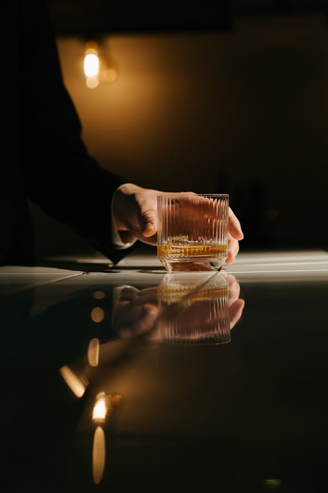 A person holding a glass of whisky in a dimly lit room.