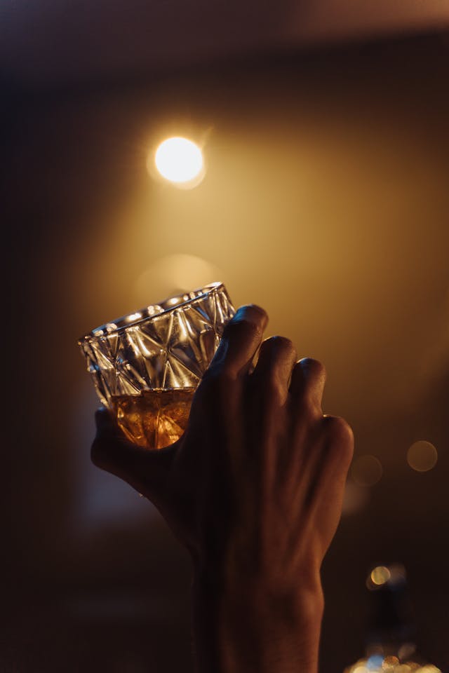 A close-up view of a person holding a glass of whisky in a dimly lit room.