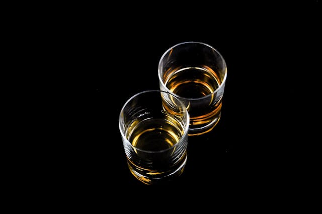 Two clear glasses filled with Indian whisky against a black background.