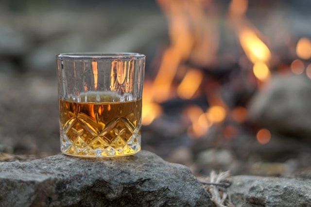 A vintage crystal glass of Australian whisky sitting on top of a rock by an outdoor campfire.