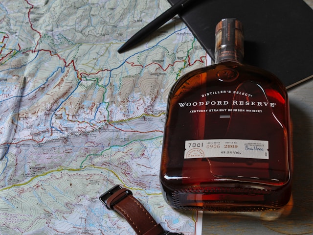 A bottle of bourbon whiskey next to a map and a leather watch strap.