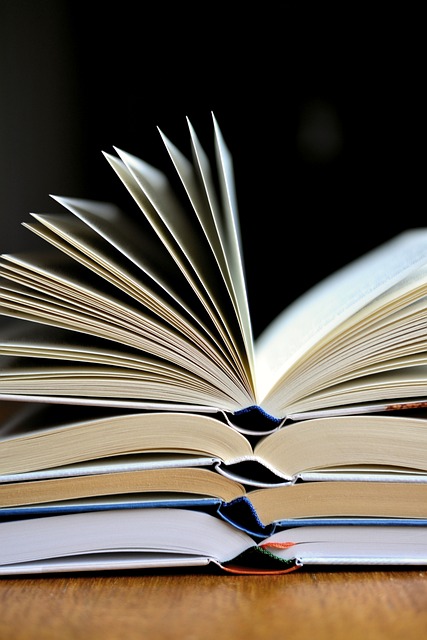 An open book with pages fanned out, stacked on two other books against a dark background.