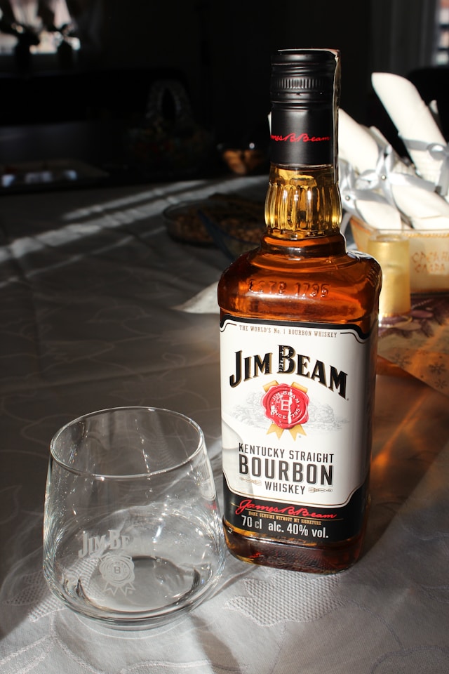 A bottle of Jim Beam bourbon whiskey beside a clear glass