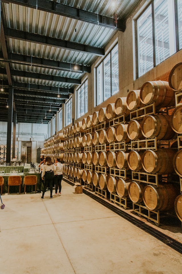 A warehouse full of wooden barrels with a few people standing in from of them.