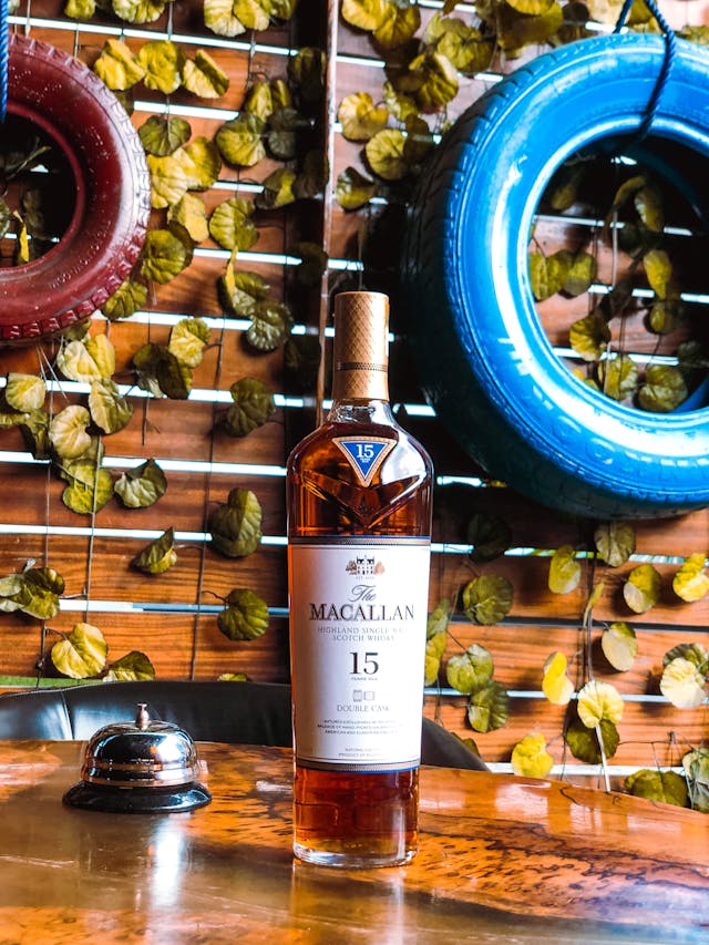 A bottle of Macallan River Spey on a wooden table with colorful tires and leaves on the background.