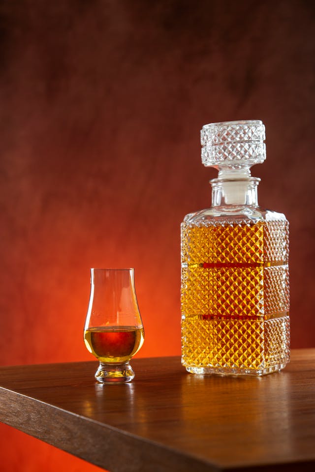 A crystal bottle of whisky and a tulip shaped glass filled with whiskey on a wooden table.
