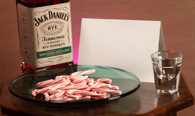 A close-up of a bottle of Jack Daniel’s rye whisky beside a plate of candy canes and a shot glass on a table.