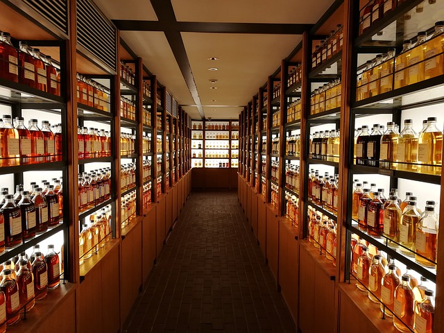 A dimly lit whisky cellar with shelves lined with bottles of whisky on both sides, leading to a bright display at the far end.