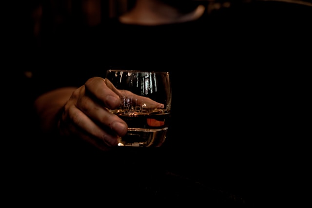 A man in black holding a glass of whisky.