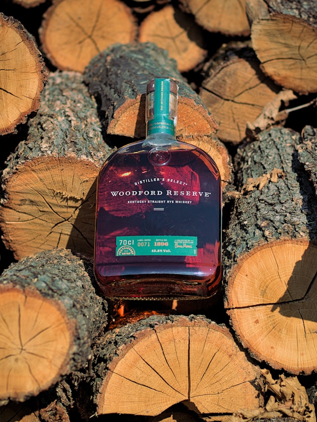 A bottle of Rye Whiskey lying among stacked logs.