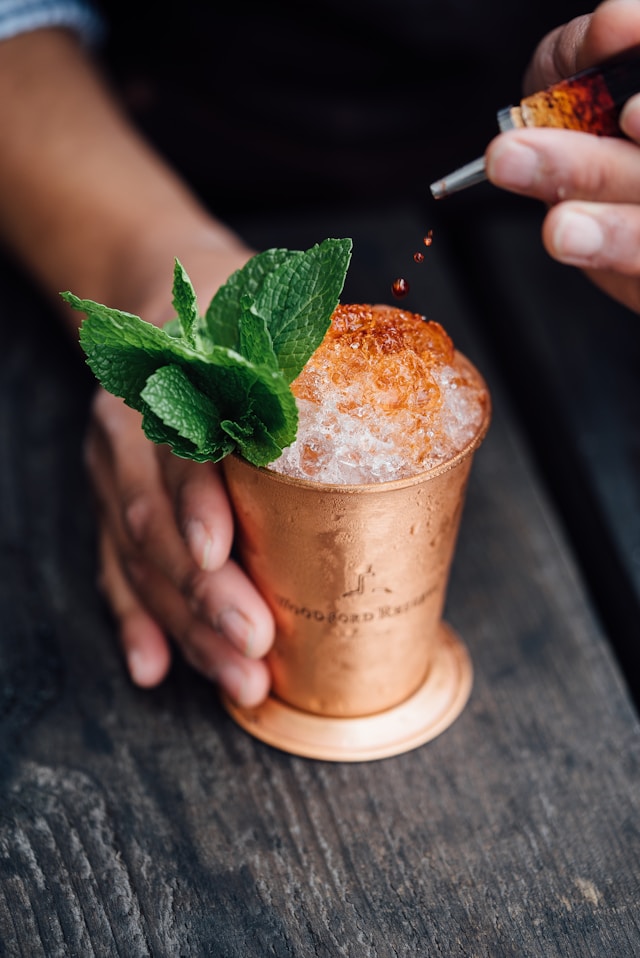 A person garnishing Mint Julep on a copper cup. 