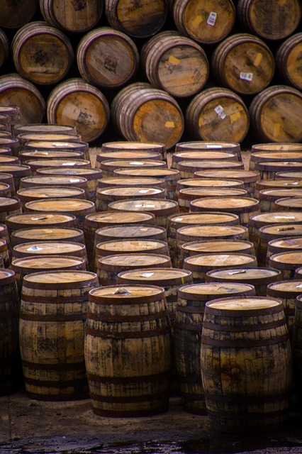 A large collection of wooden whiskey barrels stacked in rows, both upright and on their sides, in an outdoor storage area.