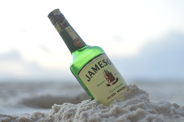 A bottle of Jameson Irish Whiskey partially buried in the sand on a beach.