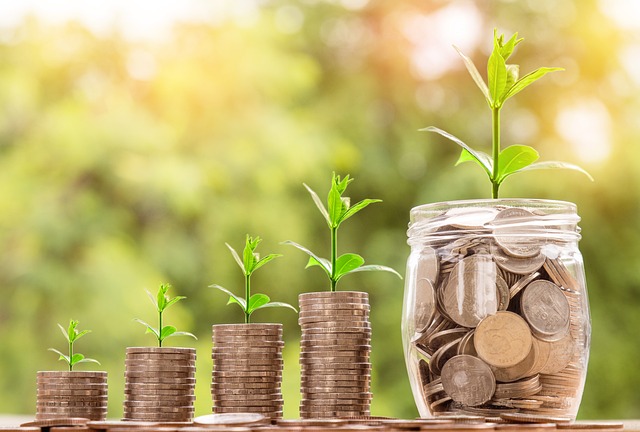 Stacks of coins with small plants growing on top, next to a jar filled with coins, symbolizing financial growth.