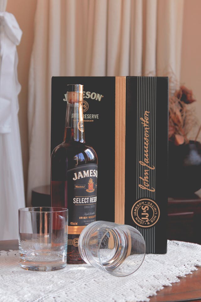 A bottle of Jameson Select Reserve Irish whiskey with its packaging, accompanied by two whiskey glasses on a wooden table.