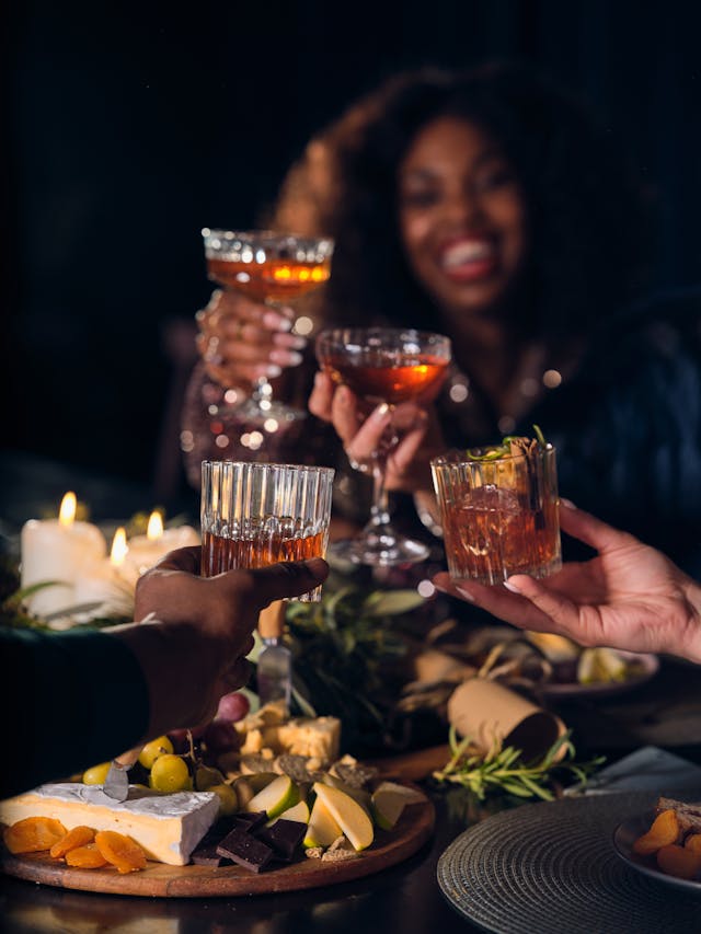 A group of people raising glasses of whisky in a celebratory toast around a table set with a cheese and fruit platter.