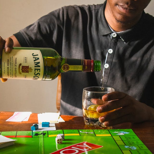 A person pouring Jameson Irish Whiskey into a glass while sitting at a table with a Monopoly board game.