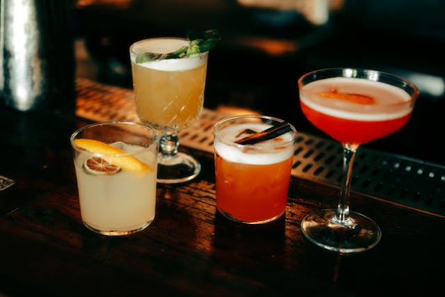 Four whiskey cocktails on a wooden bar top, each with unique garnishes in various glass styles.