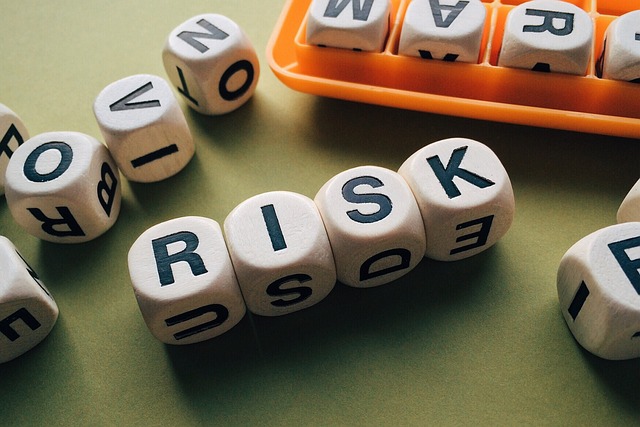 Wooden cubes spelling "RISK" with scattered letter cubes nearby, some stored in an orange tray.