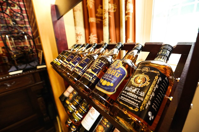 Bottles of whiskey displayed in a wooden rack, lined up at an angle in a warmly lit room with decorative curtains in the background.