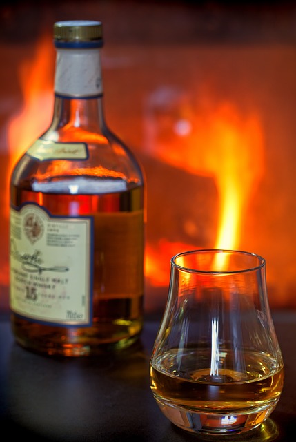 A bottle of whisky and a glass filled with whisky set against a glowing fireplace background.