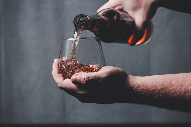 A person pouring whisky into a glass, with both hands visible holding the bottle and the glass.