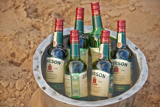 A metal bucket filled with several bottles of Jameson Irish Whiskey, set on a sandy surface.