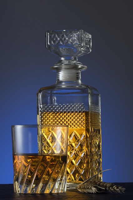 A crystal decanter filled with whisky, with a diamond-patterned design, next to a matching tumbler glass containing whisky. 