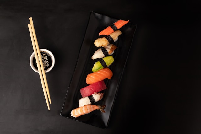 Assorted sushi on a black plate with chopsticks and soy sauce.