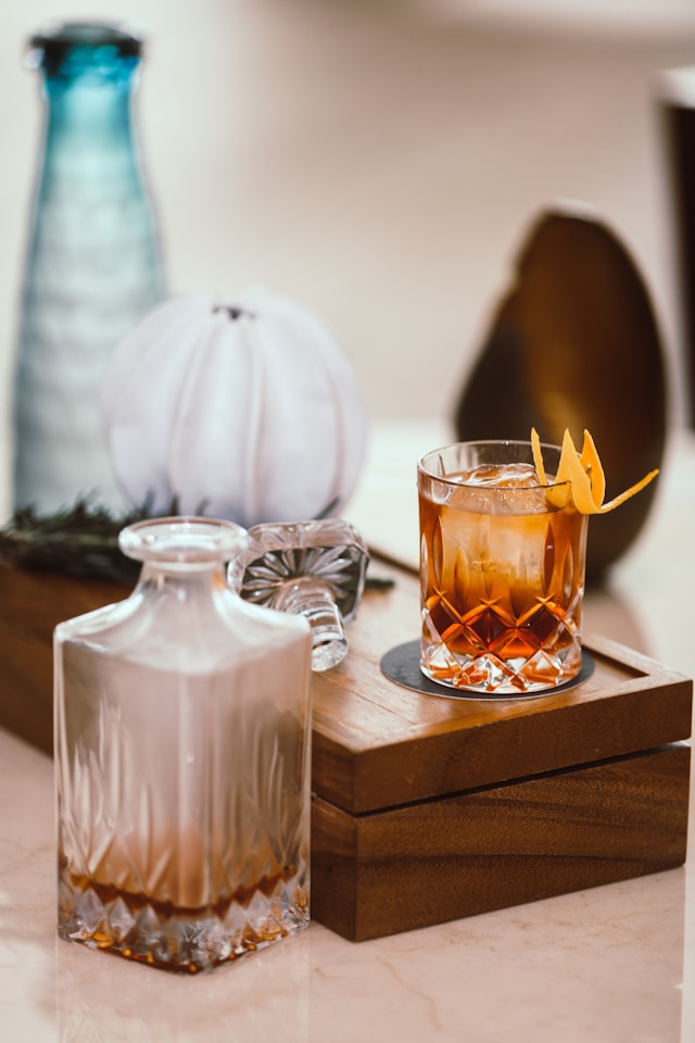 A glass of whiskey on a wooden tray alongside a crystal decanter in a cozy setting.