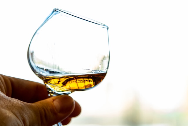 A close-up of a hand holding a whiskey glass, highlighting the amber hues of the spirit.